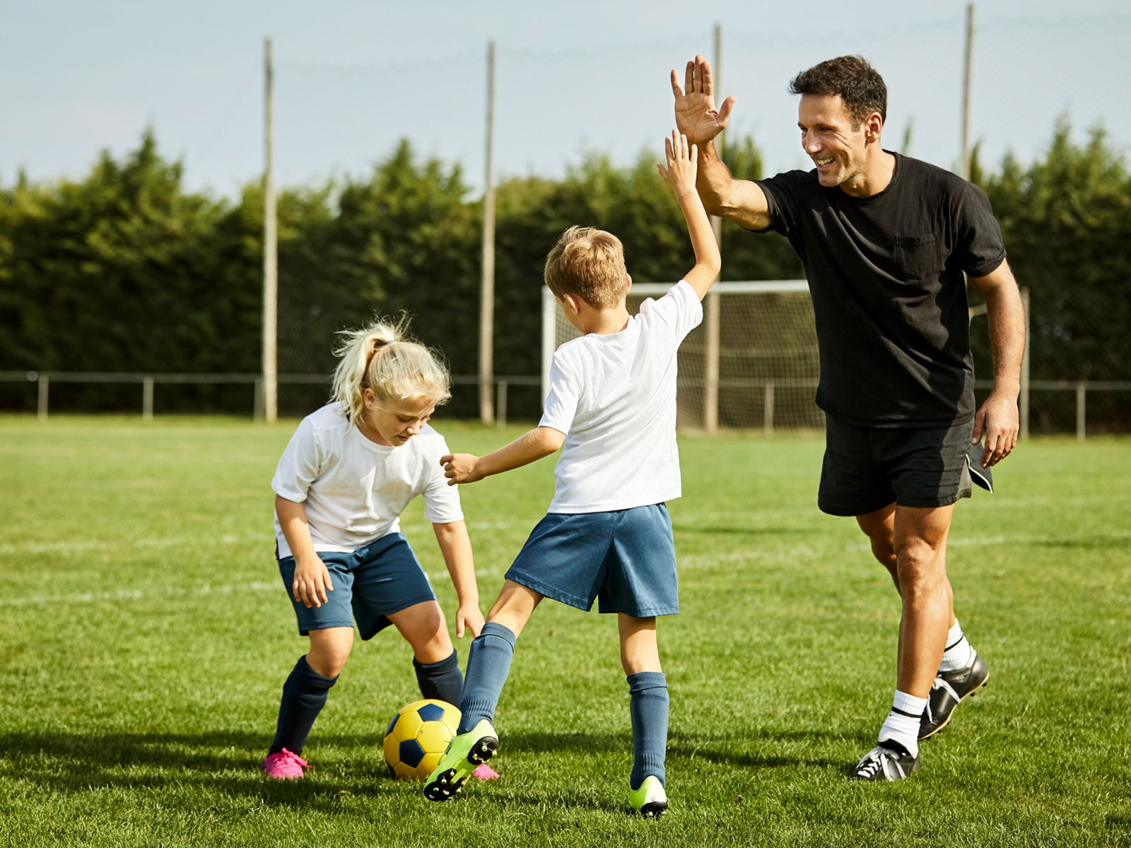 Coach plays soccer with a young boy and girl.