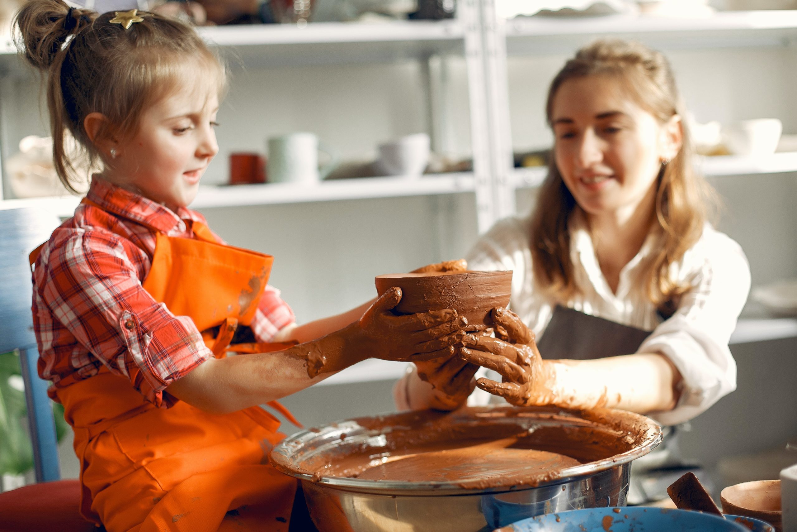 Mom and young daughter doing pottery together, shaping a clay bowl