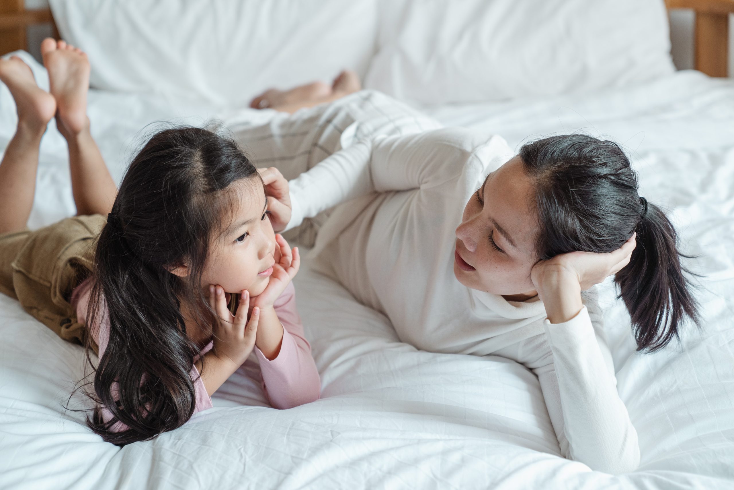 Mother and daughter lying on bed talking to each other