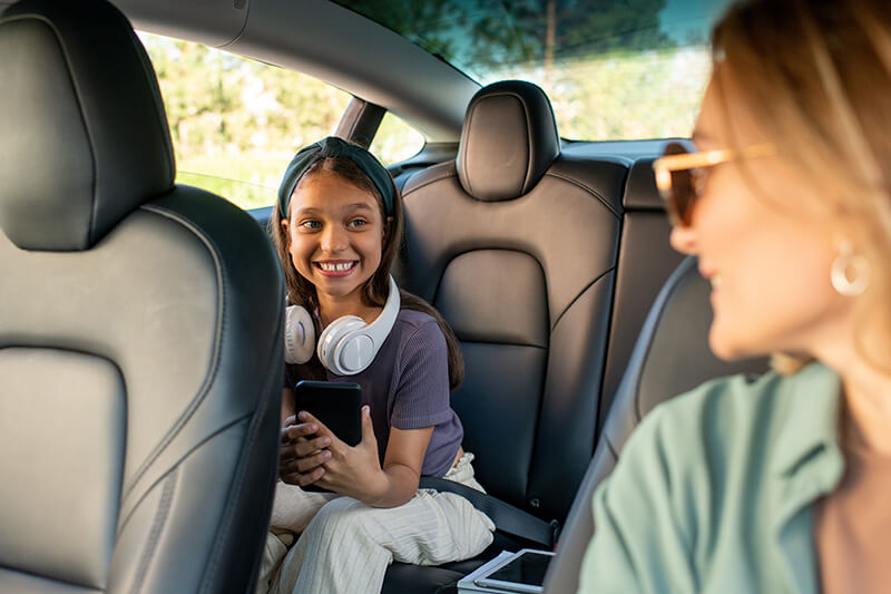 Young girl in car backseat smiling at her mom who's driving