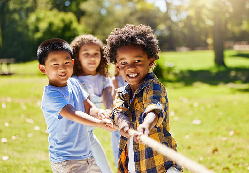 Three young kids playing tug-of-war in a park