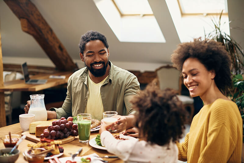 Happy African-American father, mother and child enjoying a meal at the dining table