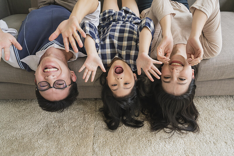 Shown from above, Asian father, mother and daughter playfully smiling at the camera